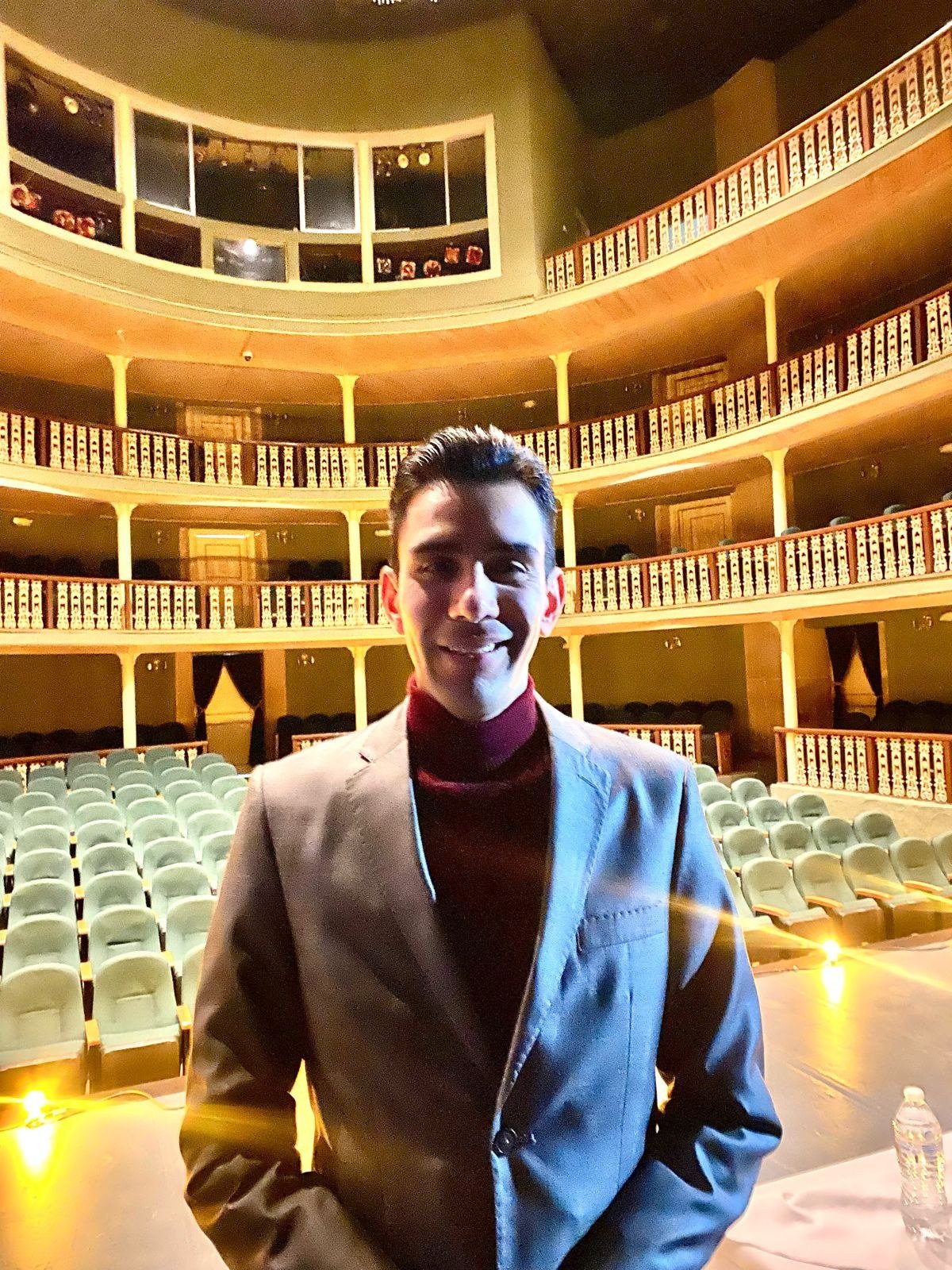 Emmanuel Meraz de pie en el escenario de un teatro, frente a las butacas vacías