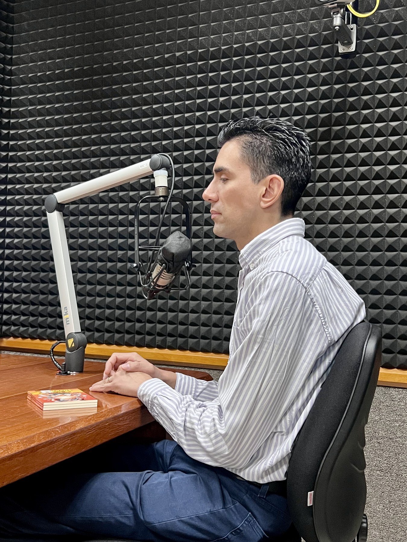 Emmanuel Meraz sentado frente a un micrófono profesional, en una cabina de radio