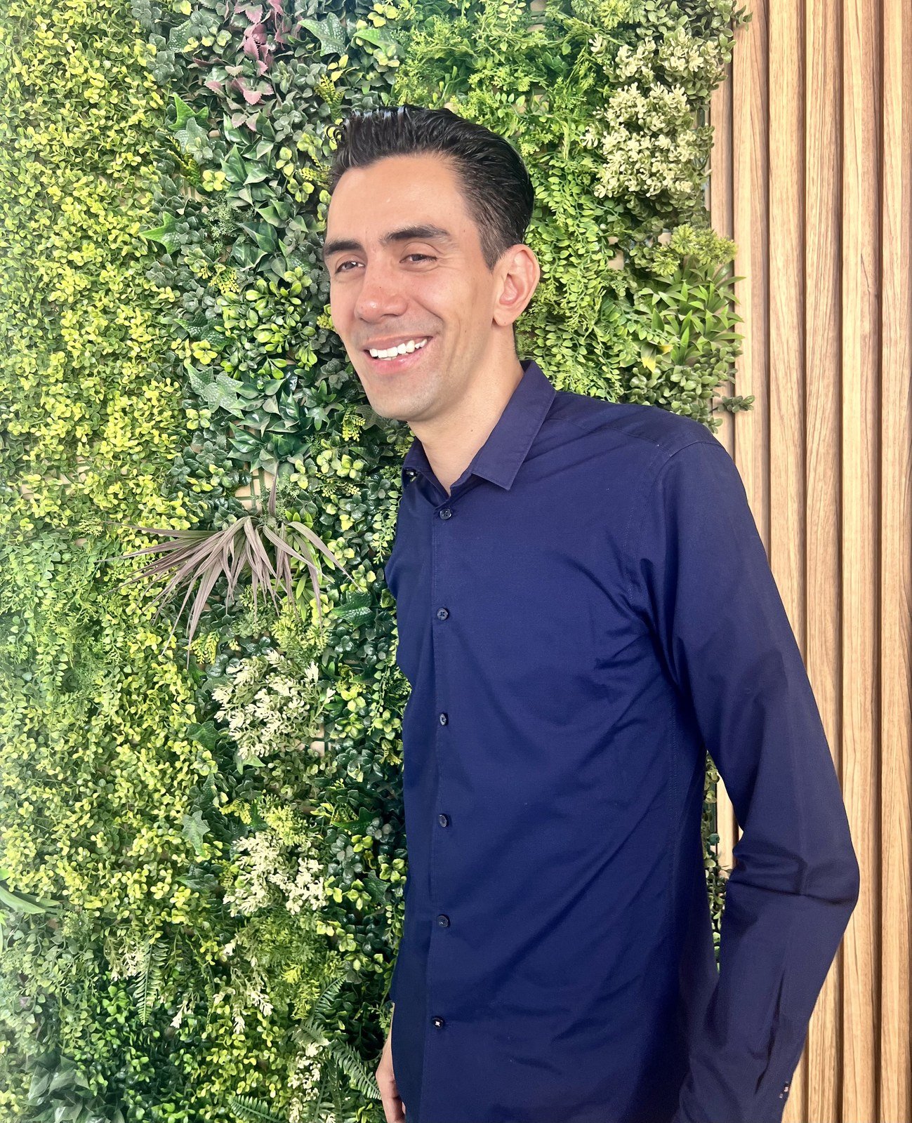 Emmanuel Meraz sonriendo, frente a un muro de plantas